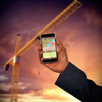 Hands of man and woman holding mobile phones  against 3d image of yellow crane against cloudy sky