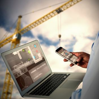 Businessman using mobile phone and laptop against 3d image of yellow crane against cloudy sky