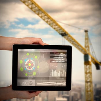 Close-up of hands holding digital tablet against 3d image of yellow crane