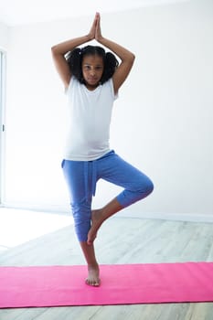 Portrait of girl doing tree pose yoga while exercising against wall in room