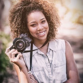 Portrait of happy woman standing in park with digital camera