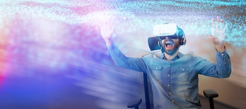 Cheerful man using virtual reality glasses while sitting on armchair against abstract glowing black background