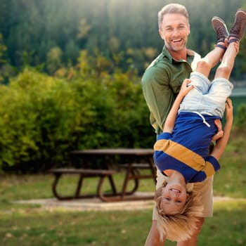 Father holding son upside-down  against bench beside lake in forest park