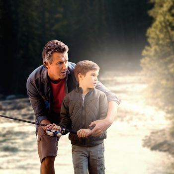 Father teaching his son fishing  against river flowing through forest