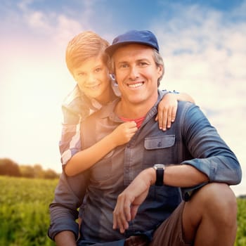 Portrait of a crouching father beside son  against view of green field and blue sky against forest background 