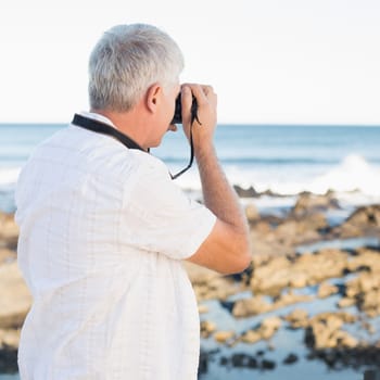 Casual mature man taking a photo of the sea on a sunny day