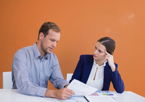 Digital composite of Business people at a desk looking at a paper against orange background