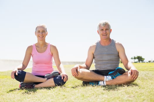 Fit mature couple sitting in lotus pose on the grass on a sunny day