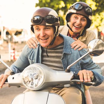 Happy mature couple riding a scooter in the city on a sunny day