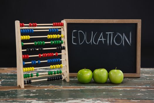 Education text on chalkboard with abacus and green apples on wooden table