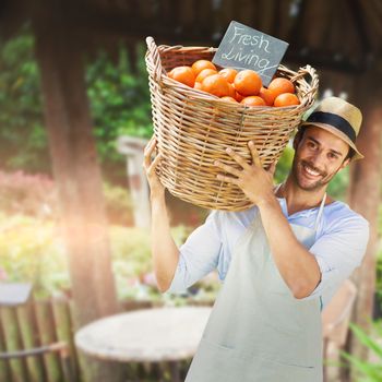 Smiling man carrying orange fruits in wicker basket against garden with furniture