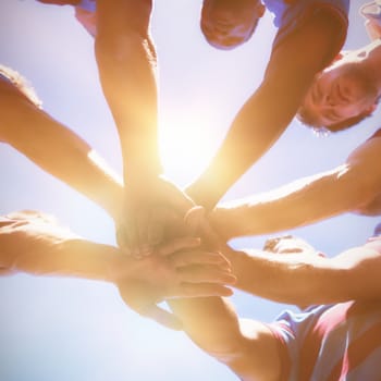 Low angle view of rugby team holding hands while standing against clear sky