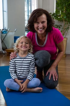 Portrait of smiling girl and physiotherapist on yoga mat in clinic