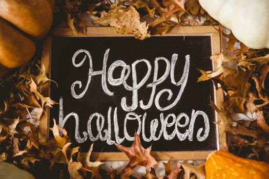 Overhead view of happy halloween text on slate amidst autumn leaves