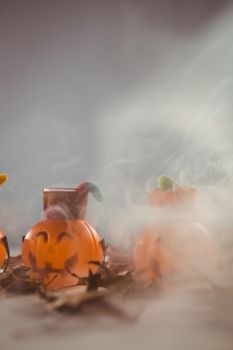 Jack o lantern containers with autumn leaves over smoke on table