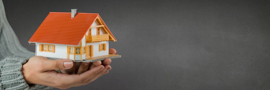 Digital composite of Woman holding a house against grey background as concept of insurance