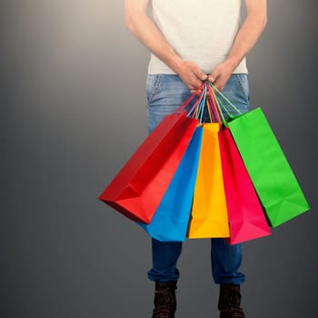 Low section of man carrying colorful shopping bag standing against white background against dark grey background