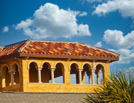 Top of a stucco building arches and a tile roof under a blue sky