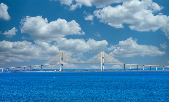 A white suspension bridge over a blue shipping channel