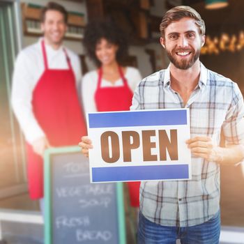 Portrait of male owner holding open sign against smiling colleagues posing behind a chalkboard
