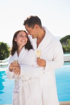 Happy romantic young couple with champagne flutes by swimming pool