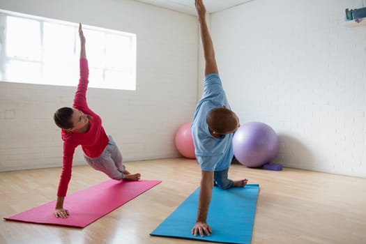Male instructor with female student practicing side plank pose in yoga studio