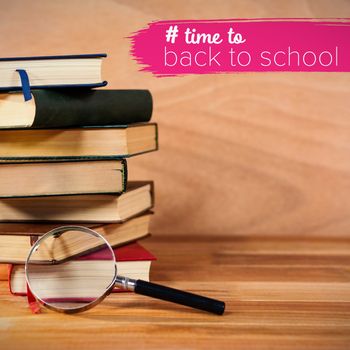 Back to school text with hashtag  against magnifying glass with stack of books on table