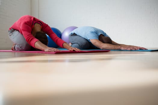 Instructor with female student practicing child pose in yoga studio