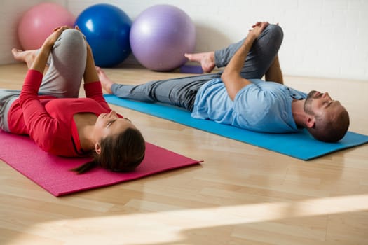 Yoga instructor and female student exercising while lying on mat in health club