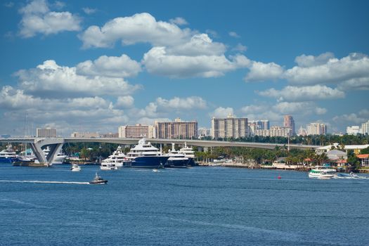 Many blue and white luxury yachts by a drawbridge in a shipping channel