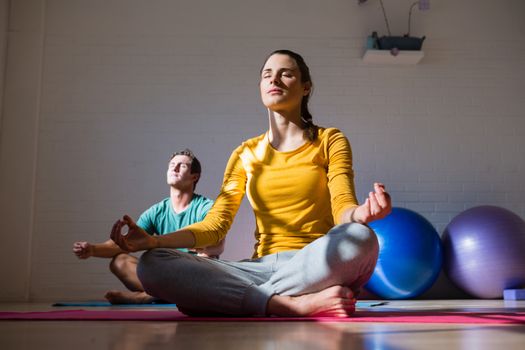 People meditating while sitting on exercise mat in health club