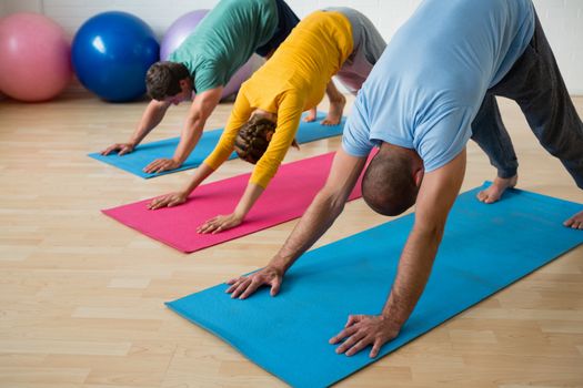 Male instructor guiding students in practicing downward facing dog pose at yoga studio