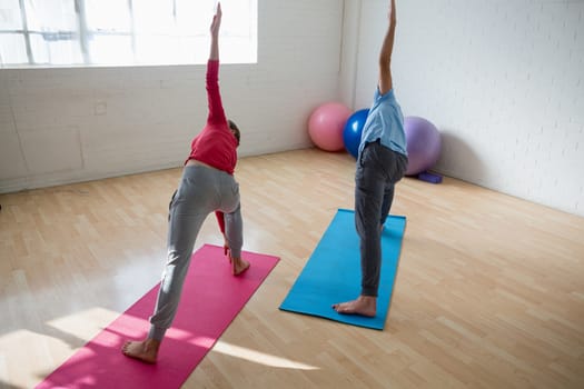 High angle view of instructor with female student practicing triangel pose in yoga studio