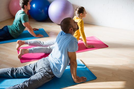 High angle view of yoga instructor with students practicing cobra pose in health club