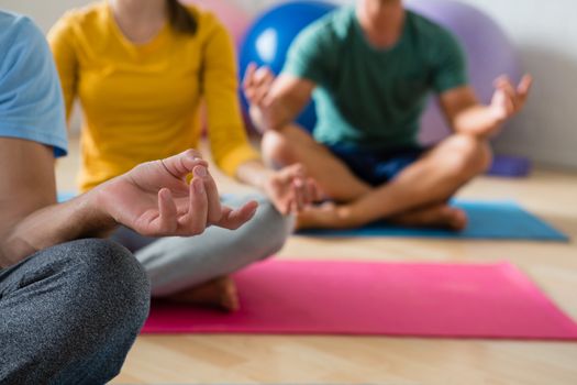 Midsection of yoga instructor with students meditating in lotus position at health club 