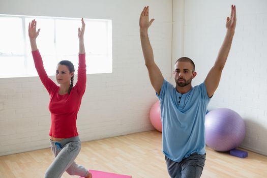 Male instructor with student practicing warrior 1 pose in yoga studio