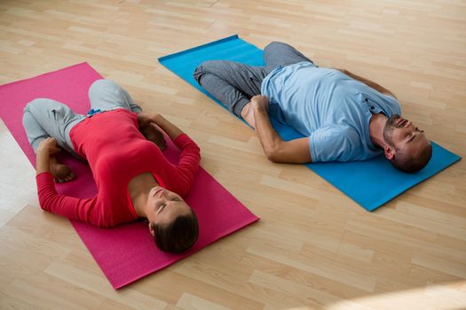 High angle view of instructor with student practicing reclined hero pose in yoga studio