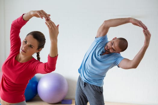 Female student with male instructor exercising in yoga studio