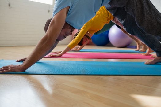 Side view of instructor with students practicing downward facing dog pose at yoga studio