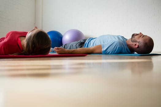 Instructor and student exercising while lying on mat in yoga studio