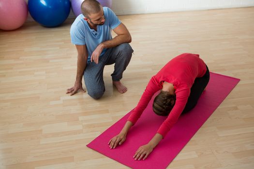 High angle view of instructor guiding student in doing child pose at yoga studio