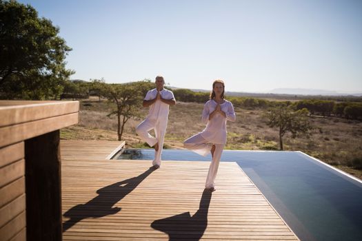 Couple practicing yoga on wooden plank on a sunny day