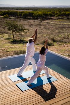 Couple practicing yoga on at poolside on a sunny day