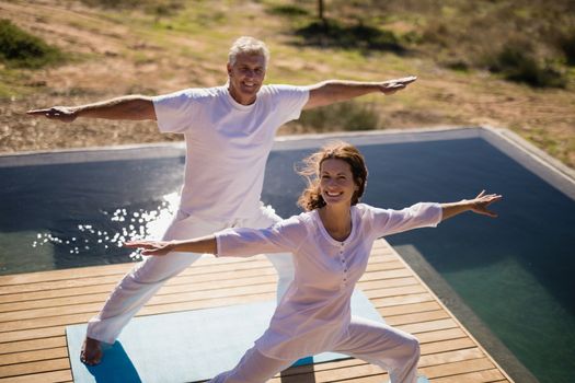 Portrait of happy couple practicing yoga on at poolside on a sunny day