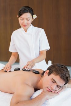 Side view of a handsome young man receiving stone massage at spa center