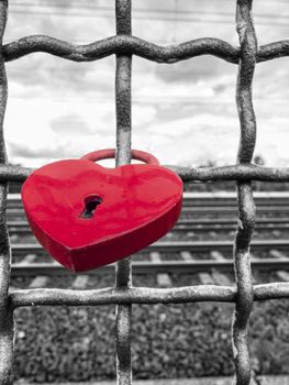 Red heart-shaped rusty padlock chained to a railing at the monochrome background.