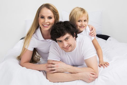 Family portrait of parents and son laying together in bed and smiling