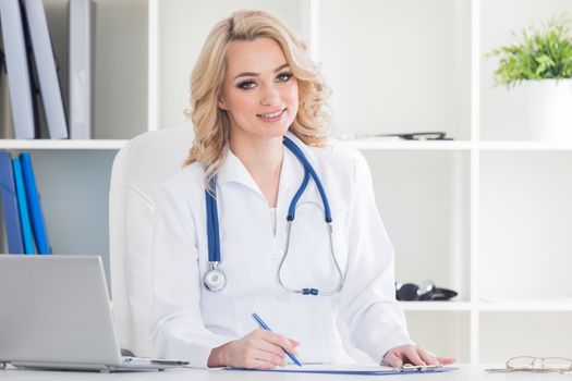 Young therapeutis female doctor writing prescription at desk in hospital office