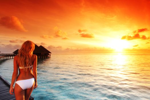 Happy young woman at beautiful water villa at Maldives island at sunset. Travel vacation tourist resort