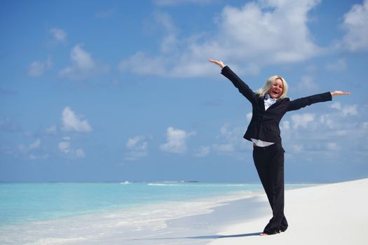 Happy business woman in formal suit with arms raised on the desolate ocean coast